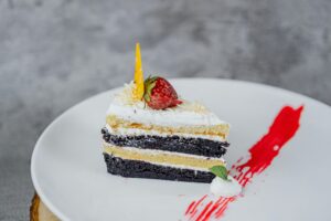 A delightful slice of layered chocolate and vanilla cake topped with a strawberry on a white plate.