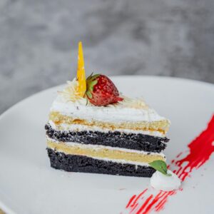 A delightful slice of layered chocolate and vanilla cake topped with a strawberry on a white plate.