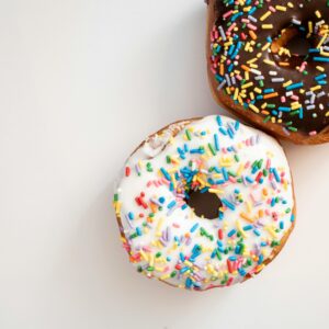 Two donuts with colorful sprinkles on a white surface, one with chocolate glaze, the other with vanilla.